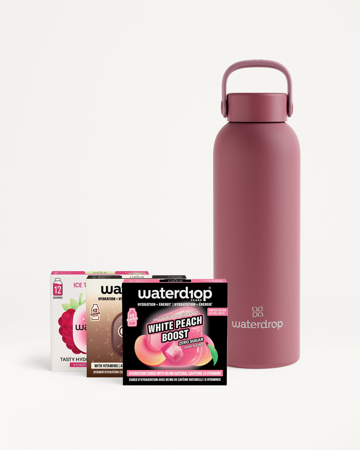 Bouteille d'eau isolante rose effet mat avec poignée, accompagnée de plusieurs sachets aromatisés.