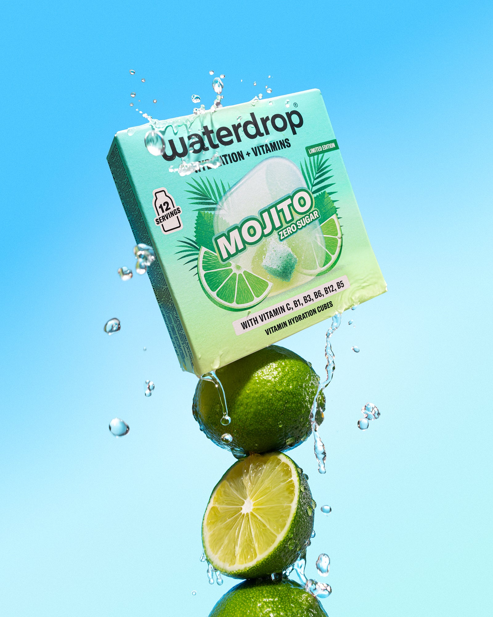 Citrons verts empilés sous une boîte vert menthe de boisson avec des éclaboussures d'eau sur fond bleu.