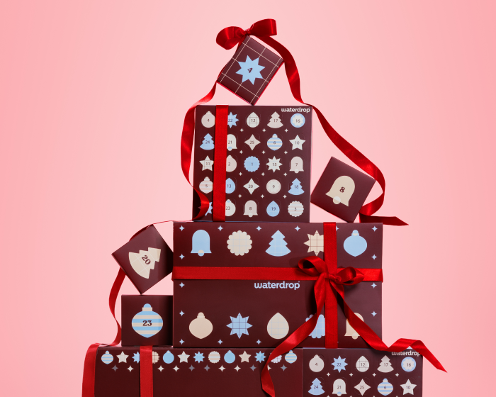 Pile de cadeaux emballés avec des motifs et des rubans rouges sur fond rose.