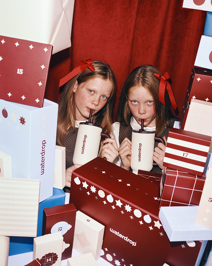 Deux filles boivent dans des gobelets blancs entourées de cadeaux colorés.