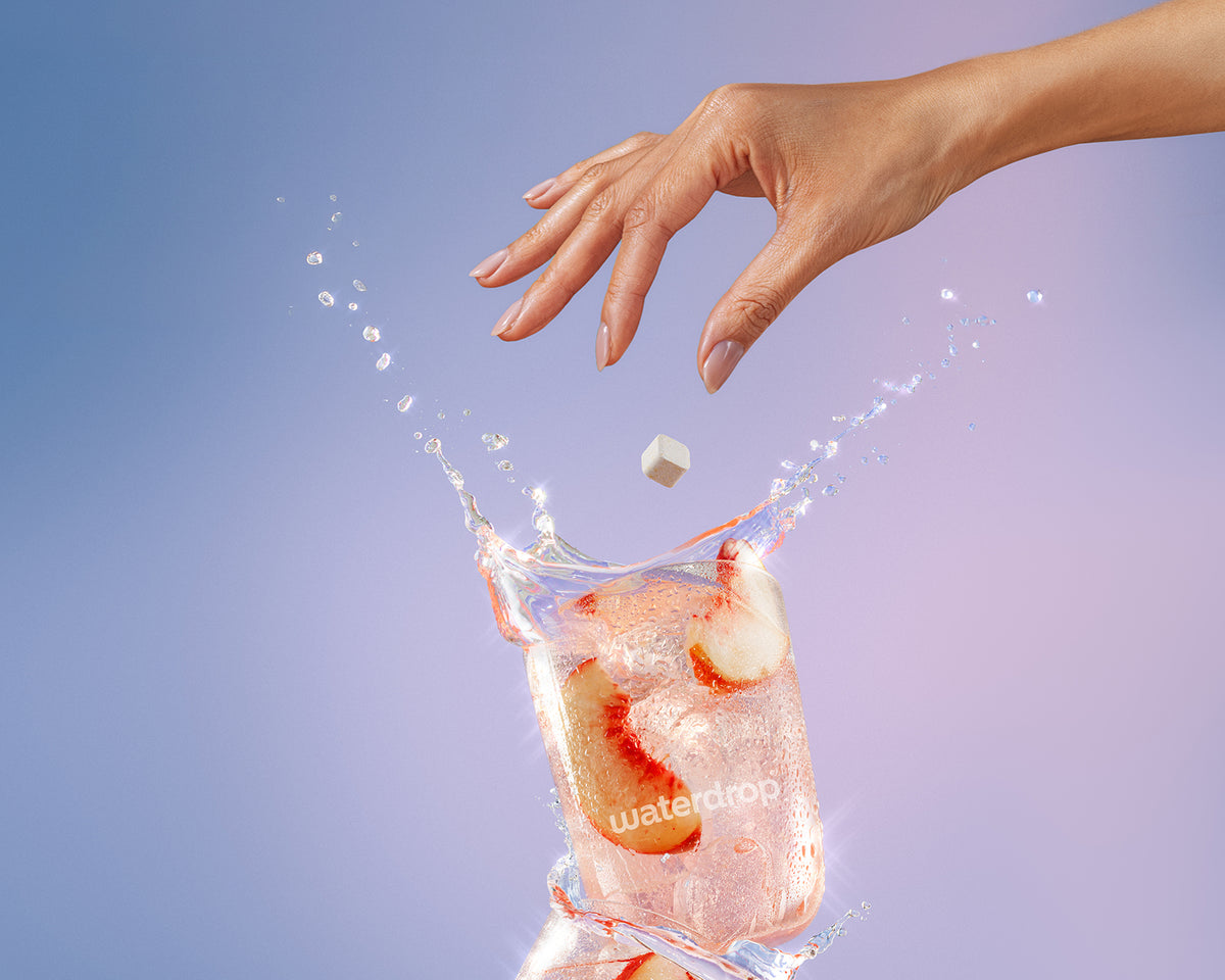 Une main laisse tomber un petit glaçon dans un verre d'eau avec des glaçons, provoquant une éclaboussure.