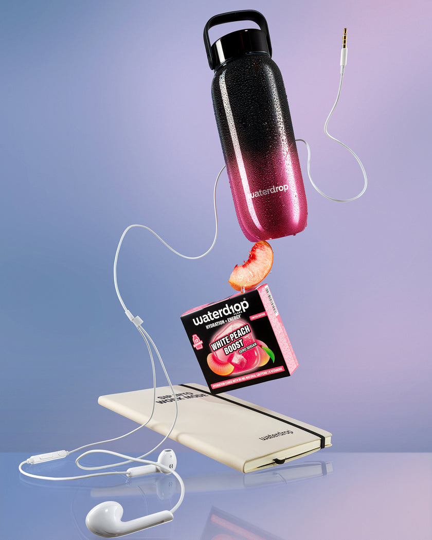 Affichage flottant d'une bouteille d'eau au dégradé noir-pourpre au-dessus d'une banque d'alimentation blanche, reliée par des câbles blancs avec une tranche de pêche à proximité.