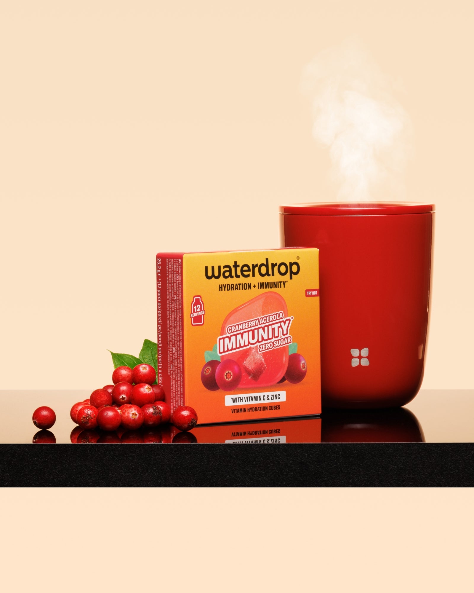 Tasse rouge fumante à côté d'une boîte rouge et d'une grappe de canneberges sur une surface lustrée.