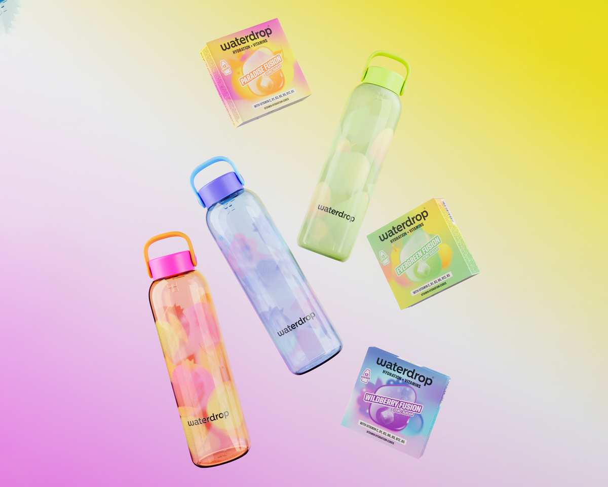 Ensemble de quatre bouteilles d'eau réutilisables transparentes avec des bouchons colorés, sur un fond dégradé pastel, avec leurs boîtes d’emballage.