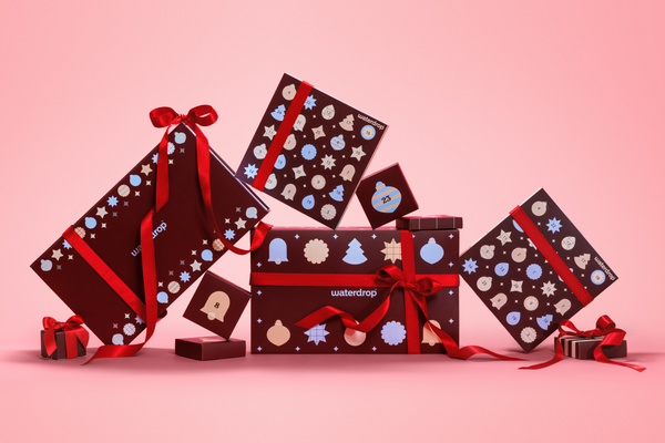 Coffrets cadeaux variés enveloppés dans du papier foncé avec des rubans rouges sur un fond rose dégradé.