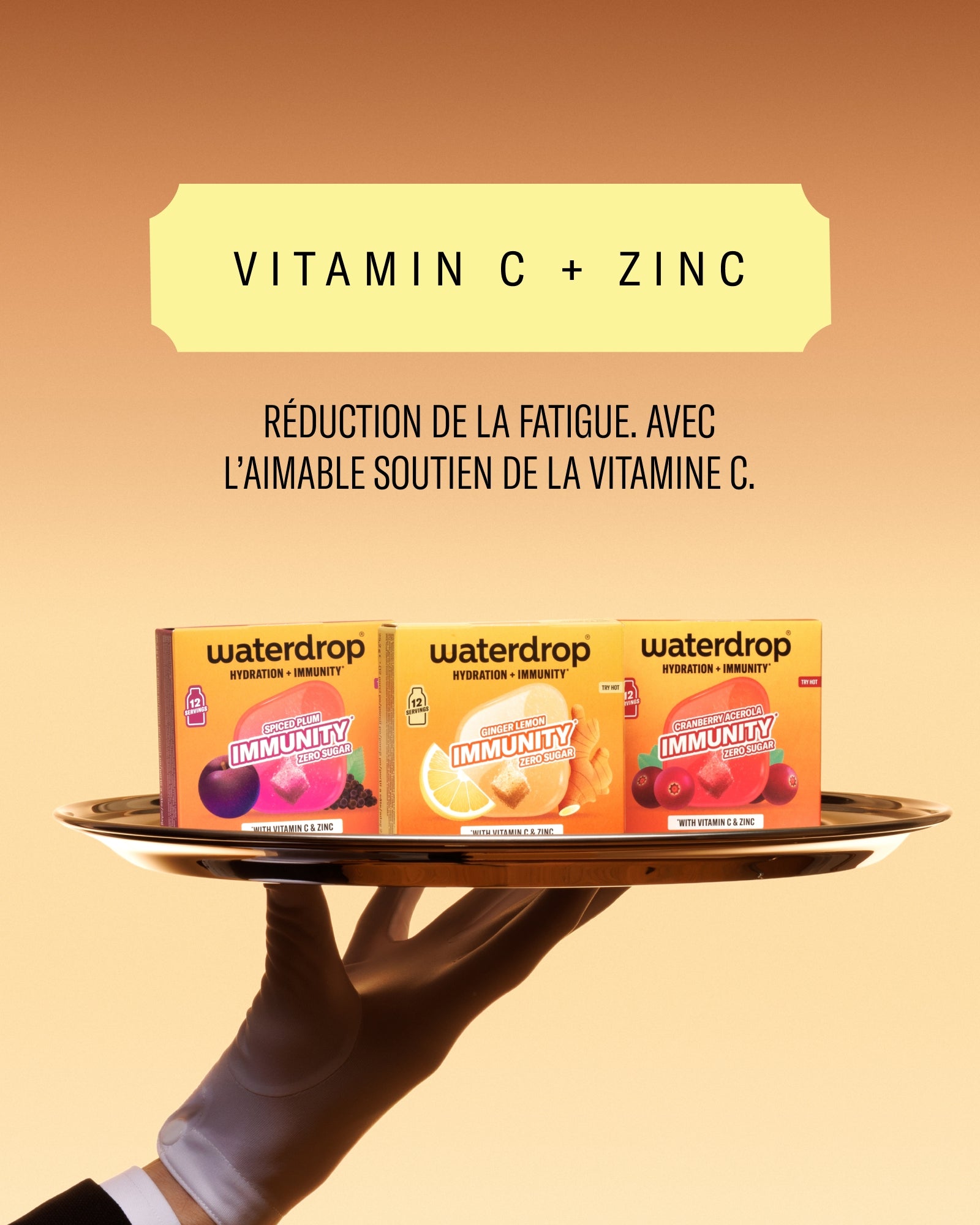 Main soutient un plateau contenant des boîtes de compléments vitaminiques contre un fond chaud en dégradé.