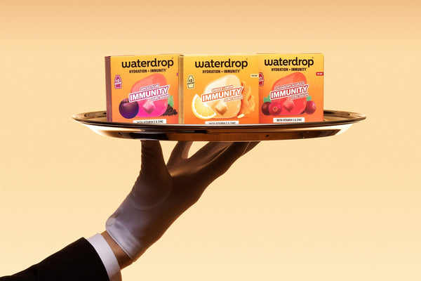 Une main gantée tient un plateau avec trois petites boîtes sur un fond orange.