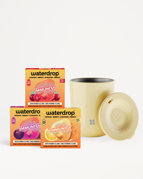 Trois boîtes de mélange vitaminiques et une tasse beige avec couvercle sur fond blanc.