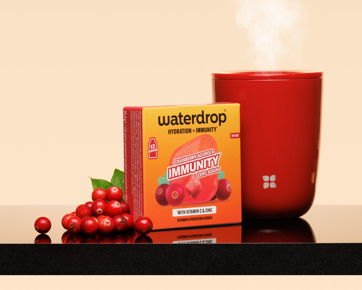 Boîte orange à côté d'une tasse rouge fumante et d’un grappin de baies rouges sur une surface réfléchissante.