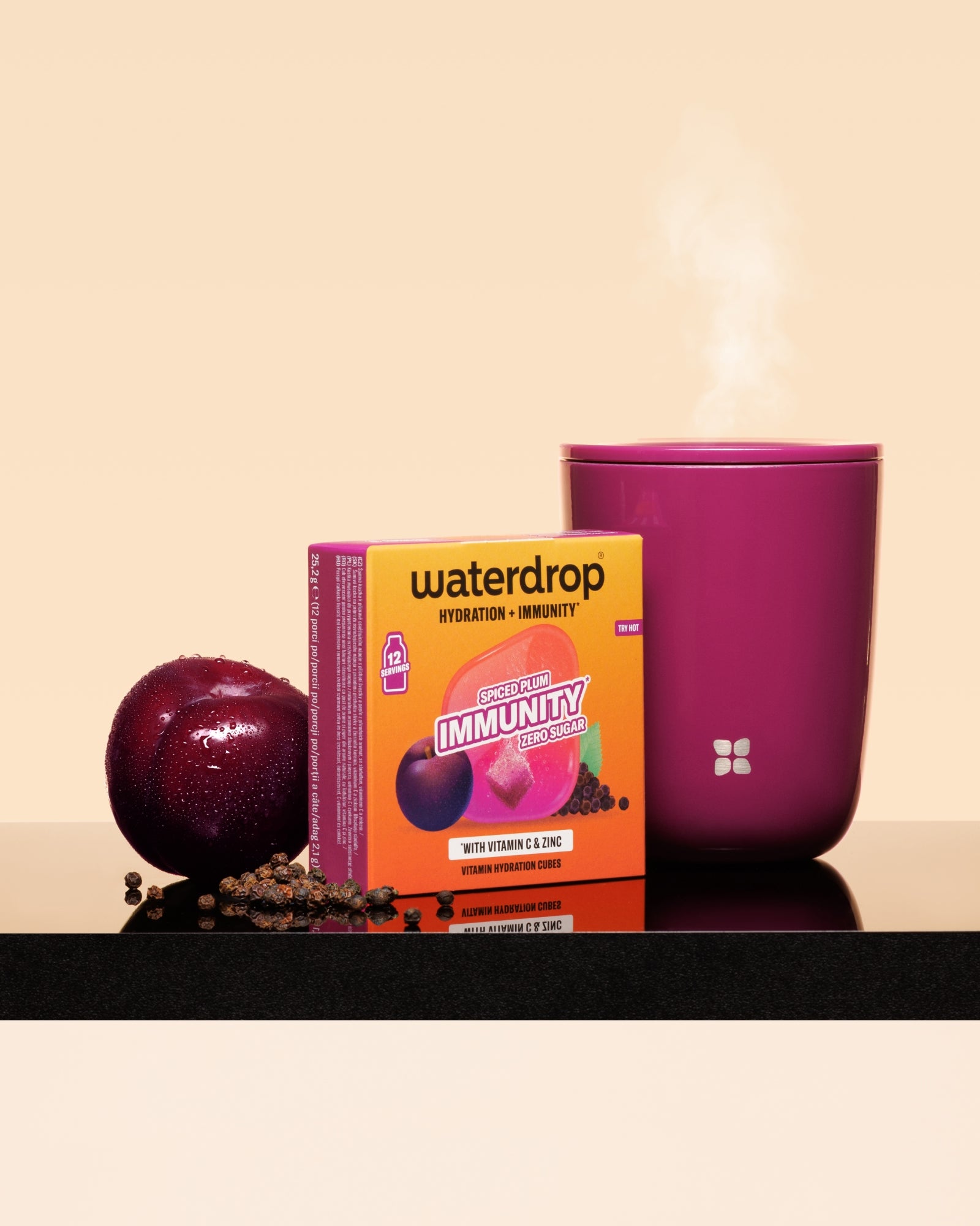 Boîte Waterdrop Immunité booster avec une prune et une tasse rose fumante sur une surface noire.
