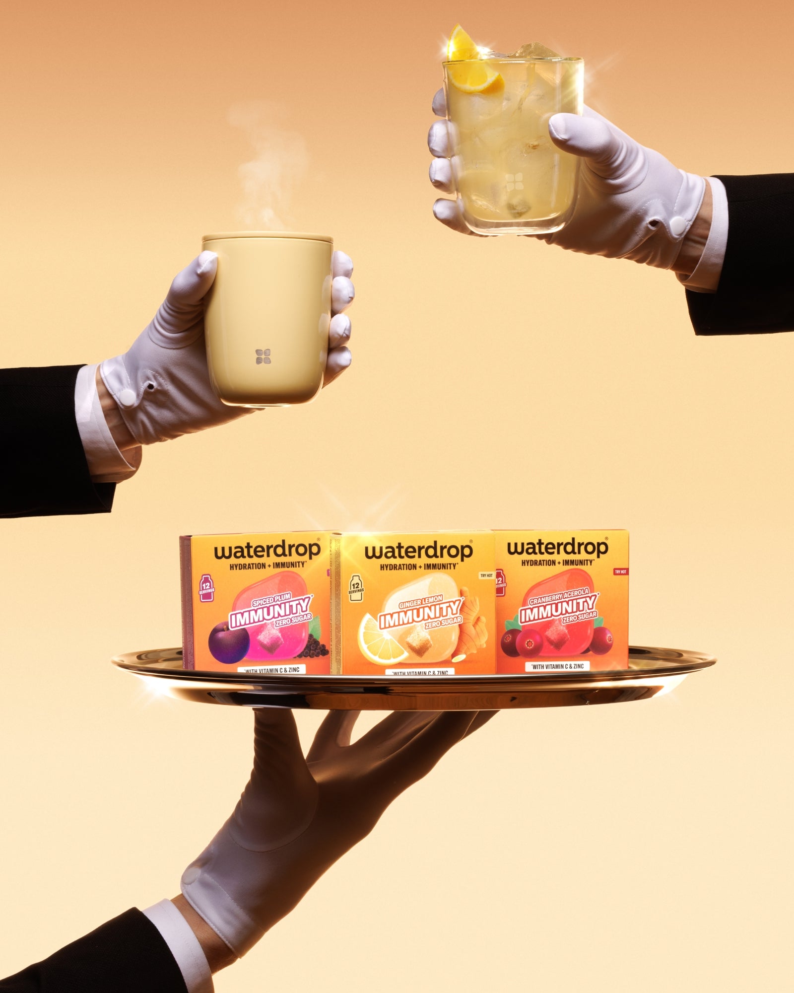 Des mains gantées présentent un plateau avec trois boîtes Waterdrop et deux tasses chaudes, sur un fond orange.