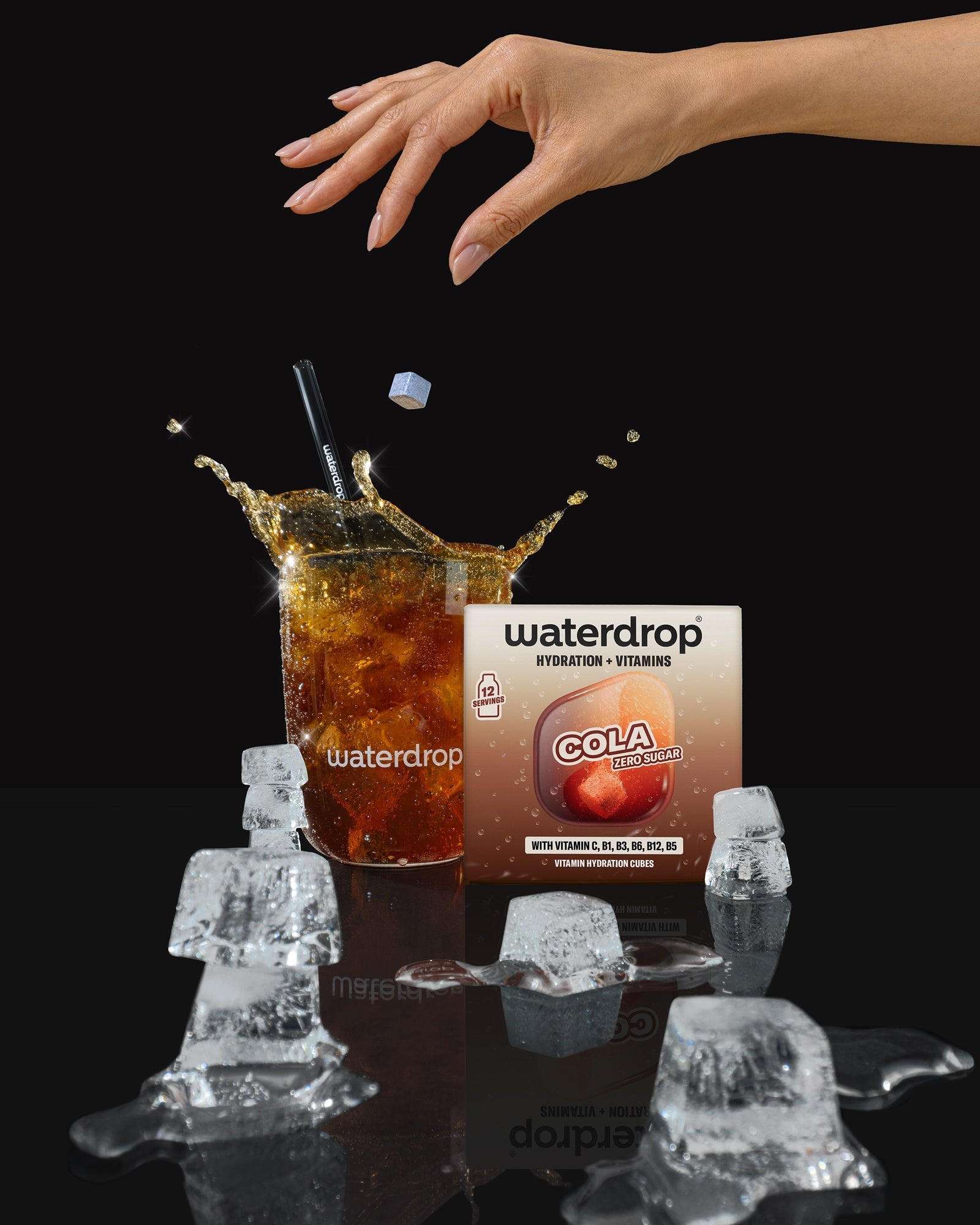 Une main s’approche d'un verre de cola avec des glaçons, une boîte de boisson est en arrière-plan.